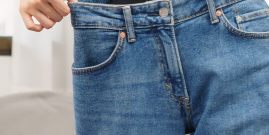 woman pulling her old jeans and showing how much weight loss she experienced